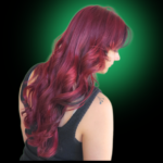 Rich, dimensional magenta and crimson red hair color. Long, layered haircut styled in soft, deep waves, showcased against a dramatic green glow background.