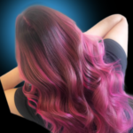 Vibrant hot pink balayage with dark plum roots on long, wavy hair. Creative vivid fashion hair color styled in soft beach waves against a blue halo light background.